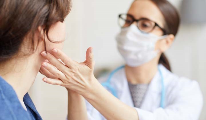 Ärztin mit Mundschutz, die eine Patientin mit Halsschmerzen untersucht Ärztin mit Mundschutz, die eine Patientin mit Halsschmerzen untersucht