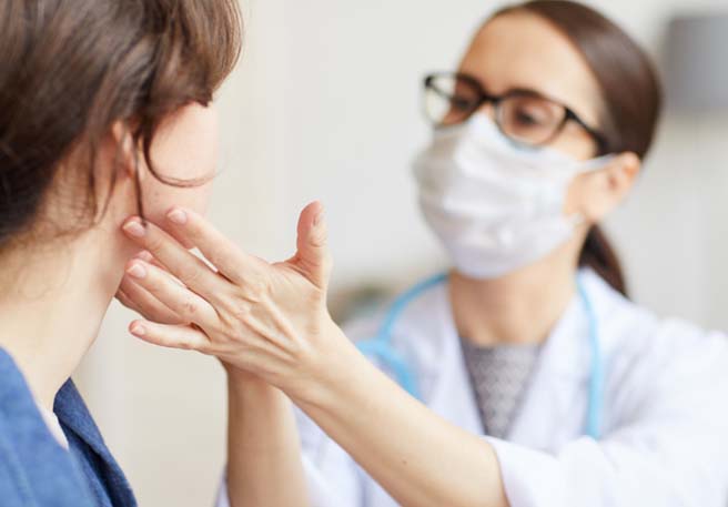 Ärztin mit Mundschutz, die eine Patientin mit Halsschmerzen untersucht