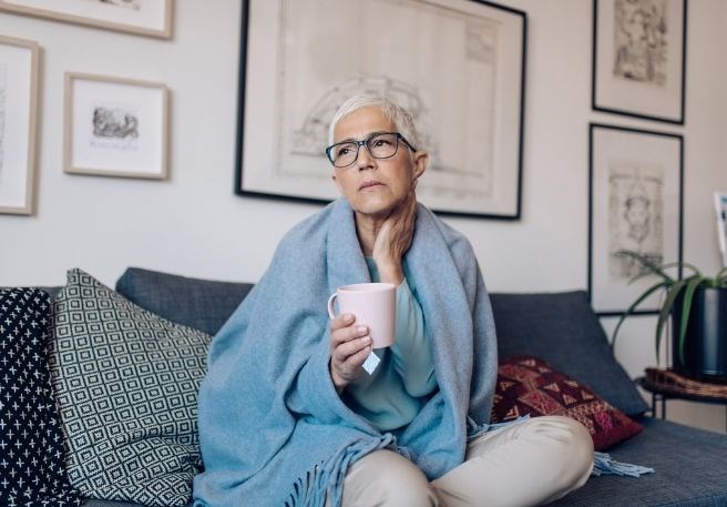 Abbildung Frau mit Halsschmerzen auf Sofa die sich an den Hals greift Abbildung Frau mit Halsschmerzen auf Sofa die sich an den Hals greift